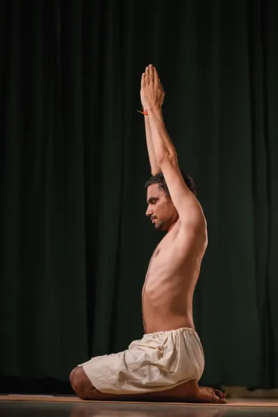 Seated on the heels with both arms raised overhead, palms joined.