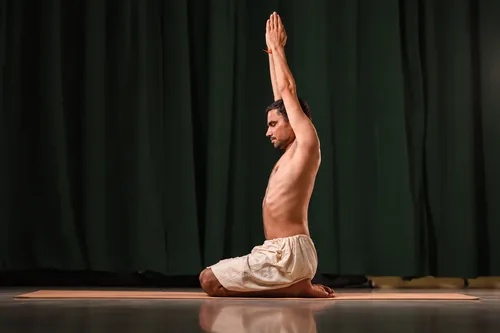 Seated on the heels with both arms raised overhead, palms joined.