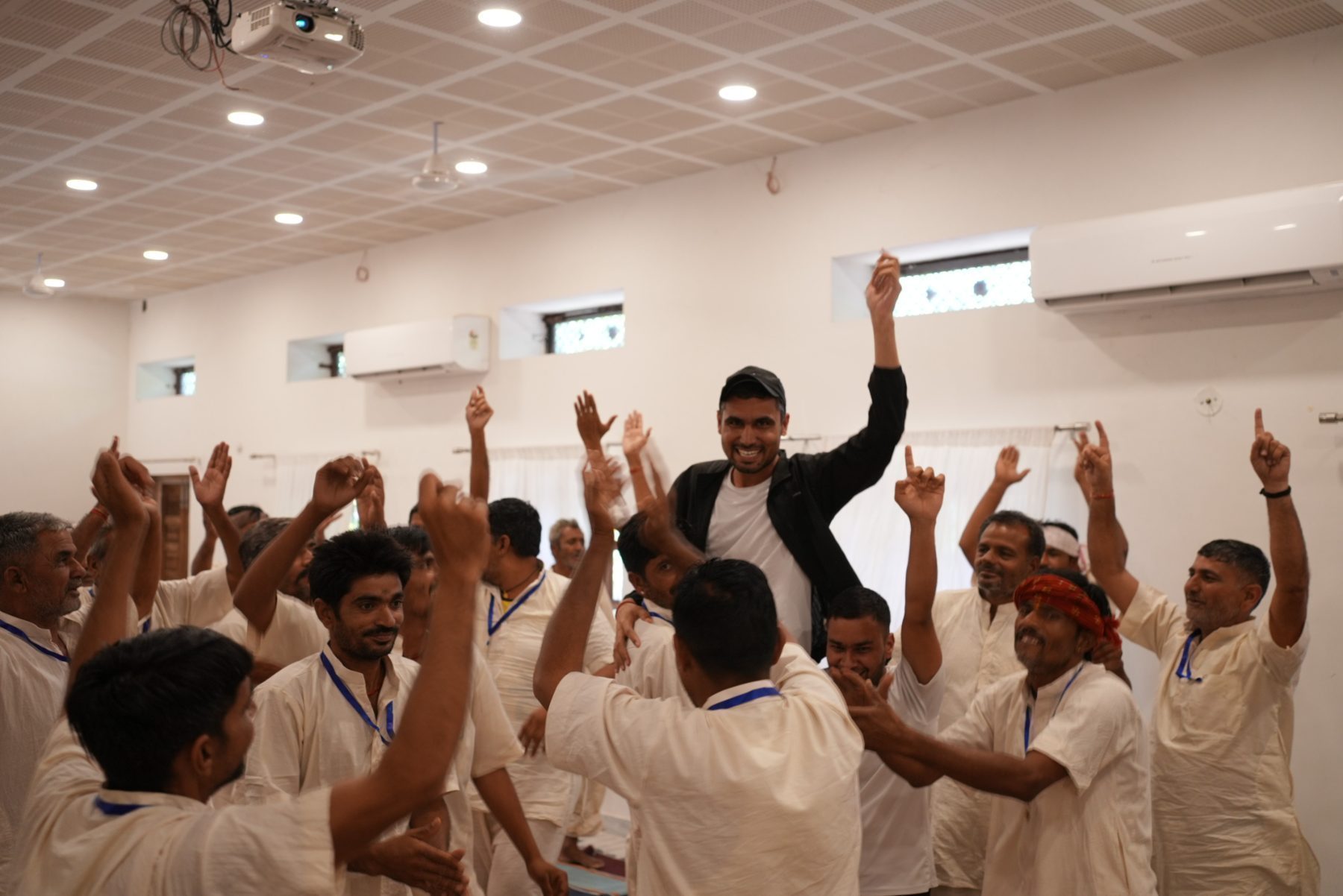 Inside a hall, a member of the team lifted up on the shoulders of participants, everyone with their arms raised and shouting.
